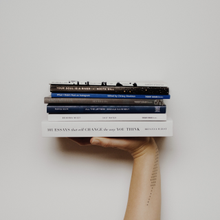 Небольшая стопка книг лежит на ладони на фоне стены.